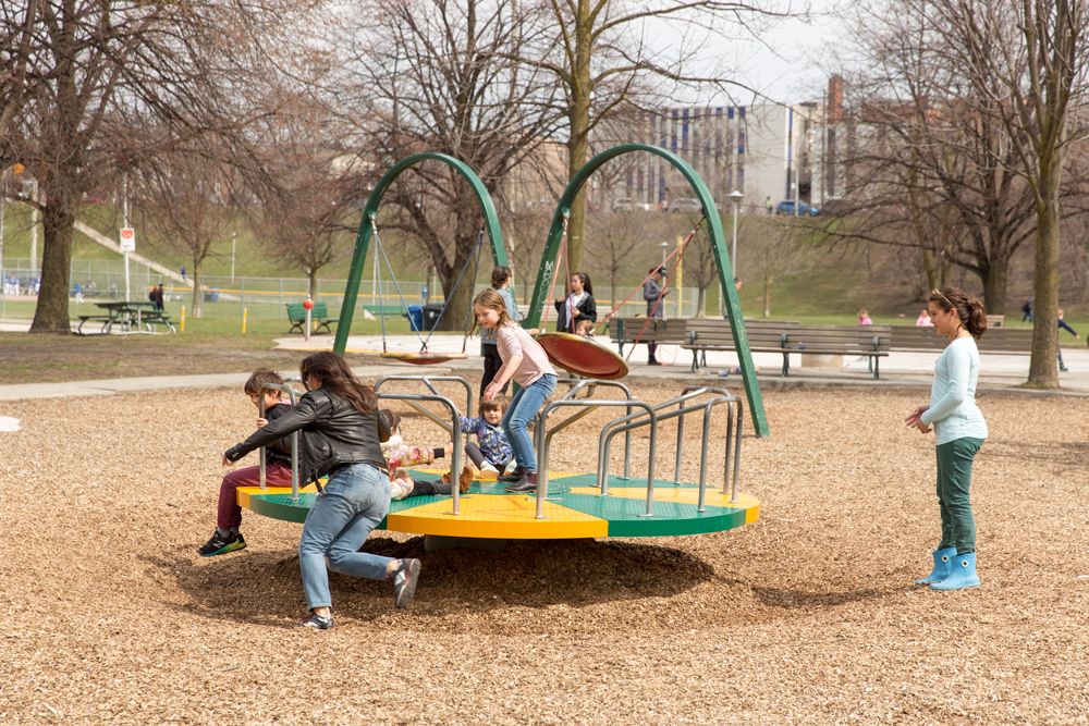 Enfants et adultes jouant sur un tourniquet au parc Christie Pits (Toronto, Ontario)